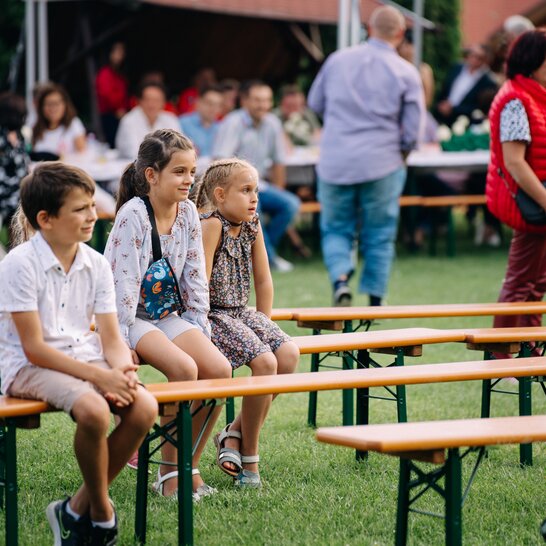 Kinder unterschiedlichen Alters sitzen auf RUKU1952 Bierbänken und blicken in die Ferne.
