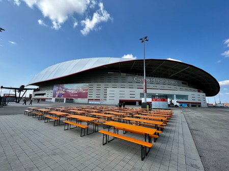 Classic beer garden table sets are set up in front of the Atletico de Madrid stadium.