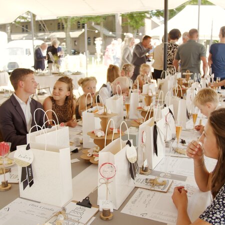 Viele Kinder sitzen an einem Tisch auf einer Bierzeltgarnitur bei einer Hochzeit.