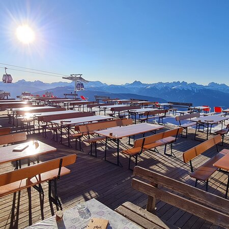 Breite Bierzeltgarnituren mit Lehne sind auf einer Alm vor einer Hütte im Winter aufgestellt.