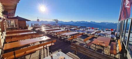 Wide beer garden table sets with backrest are placed in front of a hut in winter.