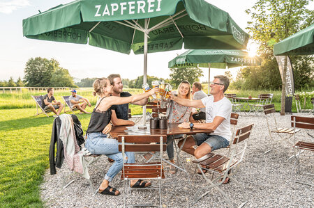 4 people are toasting with their beer on the beer garden furniture on the terrace of a pub.
