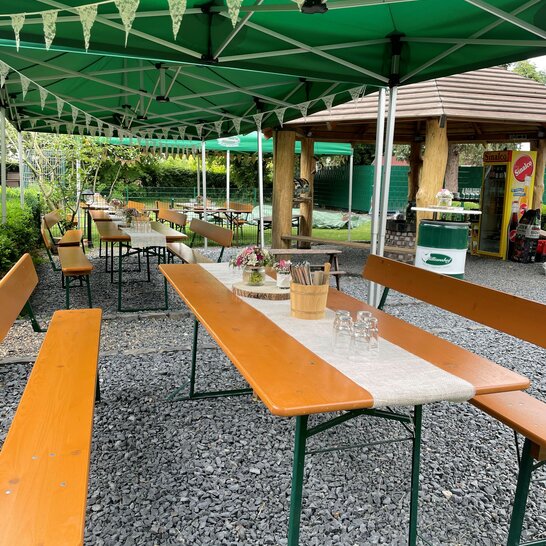 Für ein Event im Milianshof wurden breite Bierzeltgarnituren mit Lehne dekoriert und im Außenbereich unter einem Faltpavillon aufgestellt.