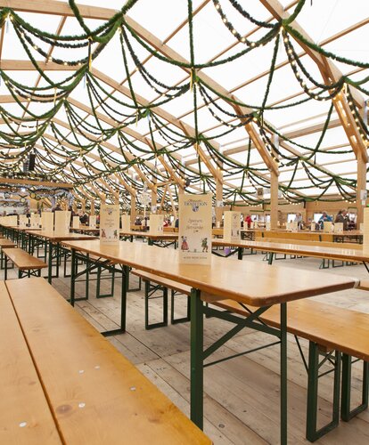 Das Bild zeigt das Innere eines Oktoberfestzeltes und darauf sieht man reihenweise aufgestellte RUKU1952 Classic Bierzeltgarnituren in der Farbe Kiefer.