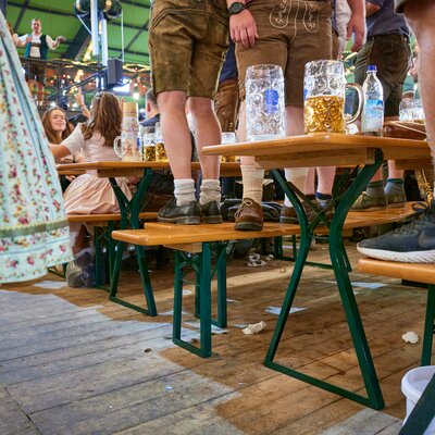 Mehrere Personen stehen beim Oktoberfest auf den Bierbänken der Bierzeltgarnitur mit Beinfreiheit.