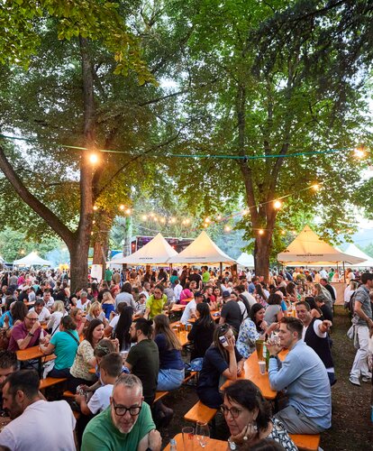 Die Besucher des Street Food Festivals haben auf den klassischen Bierzeltgarnituren Platz genommen und genießen die Veranstaltung.