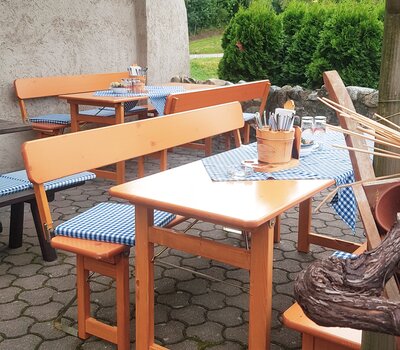 Auf dem Bild sieht man ein paar Rustica Garnituren mit Lehne, die bei dem Torggelegasthaus Trinnerhof aufgestellt wurden. Die Bierzeltgarnituren stehen in einer Laube und sind umgeben von Weinreben. Die Rustica Designgarnituren wurden gedeckt und auf den Bierbänken sind ein paar Pölster.